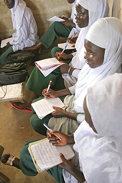 Tanji Village, African Muslim girls wearing white headscarves while attending a class at the Ousman Bun Afan Islamic school sitting in line writing in exercise books, Tanji, Western Gambia, The Gambia