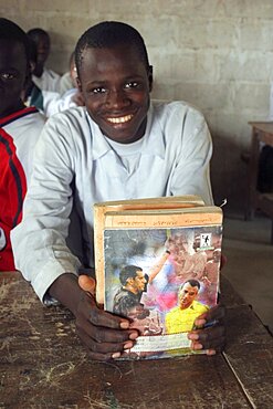 Tanji village, Smiling student from Usman Bun Afan private Islamic school proudly showing his exercise book with picture of a football referee showing a yellow card to Brazilian football player Cafu, Tanji, Western Gambia, The Gambia