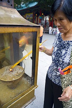 Chinese woman is lighting a candle as an offering outside of Sik Sik Yuen Wong Tai Sin temple