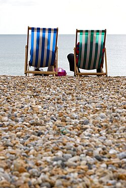 England, West Sussex, Bognor Regis, Two elderly seniors sitting on deck chairs on the pebble shingle beach looking out to sea.