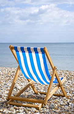 England, West Sussex, Bognor Regis, Single blue and white deck chair on the shingle pebble beach looking out to sea.