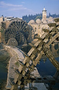 SYRIA Central Hama Wooden norias or waterwheels on the Orontes river and the Al-Nuri Mosque dating from 1172 and built of limestone and basalt.  Large section of a wheel in the immediate foreground.