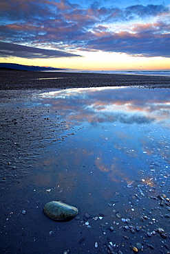 A remote west coast beach at dawn, the sunrise glistening on the Southern Alps mountain range in the distance, West Coast, South Island, New Zealand, Pacific