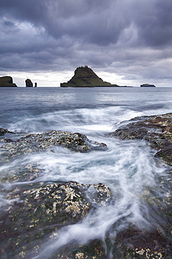 Waves swirl around the rocky seashore of Vagar, looking towards the beautiful island of Tindholmur in the Faroe Islands, Denmark, Europe 