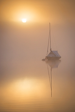 Sun rising over a sailing boat moored on a misty Wimbleball Lake, Exmoor National Park, Somerset, England, United Kingdom, Europe