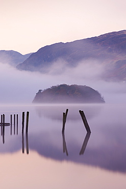 Old wooden jetty and St. Herbert's Island on Derwent Water at dawn on a misty autumn morning, Lake District National Park, Cumbria, England, United Kingdom, Europe