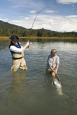 Fisherman catching a Silver (Coho) salmon (Oncorhynchus kisutch) with boy netting the fish, Coghill Lake, Alaska, United States of America, North America