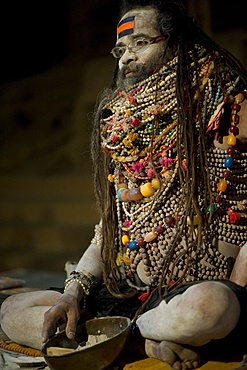 Lali Baba, a priest waiting for worshippers that he will bless with ash from the bowl at his feet, wearing necklaces given to him to worship Shiva, Varanasi, Uttar Pradesh, India, Asia