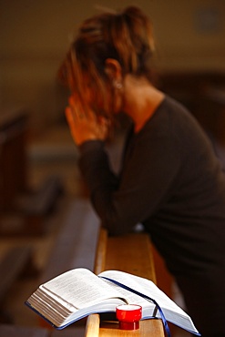 Candle and Bible, with woman praying in the background, Saint Nicolas de Veroce, Haute Savoie, France, Europe