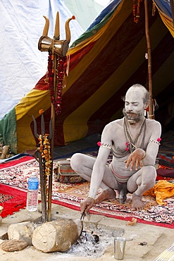 Shivaite Naga sadhu poking a sacred fire in his akhara at the Kumbh Mela in Hardwar, Uttarakhand, India, Asia