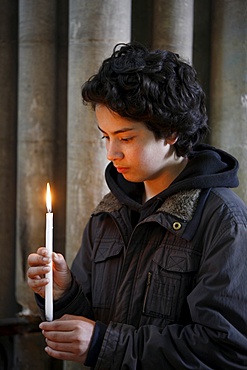 Teenager holding a candle in Notre Dame de Bayeux cathedral, Bayeux, Normandy, France, Europe