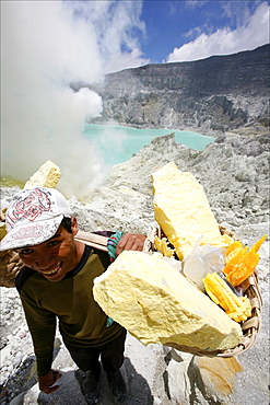 Worker carrying heavy baskets of sulphur, by the crater lake of the Kawa Ijan volcano where a sulphur mine constantly smokes, Baluran National Park, Java, Indonesia, Southeast Asia, Asia