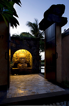 Illuminated sculptural head at dusk within a villa entrance, Baie aux Tortues, Pointe aux Pimentes, Mauritius, Africa