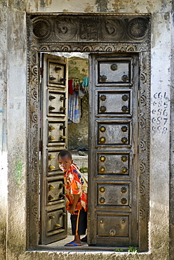 Young boy curiously looking through an old antique door, Moroni, Grand Comore, Comoros, Indian Ocean, Africa