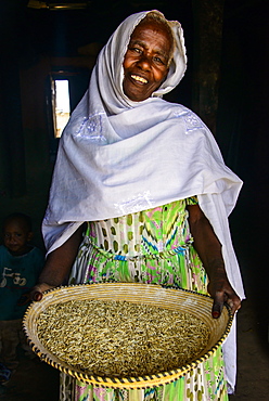 Friendly old woman standing with a basket of corn in a door frame, near Keren, Eritrea, Africa