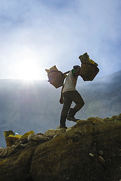 Backlit image of workers loaded with sulphur pieces cut out from a sulphur mine on Ijen crater lake, Java, Indonesia, Southeast Asia, Asia