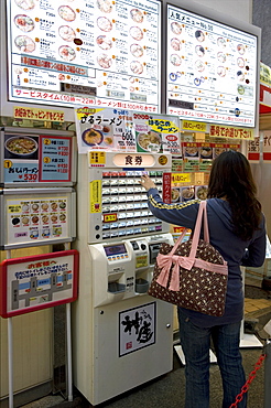 Woman purchasing meal tickets from a vending machine at a restaurant in Dotonbori, Osaka, Japan, Asia