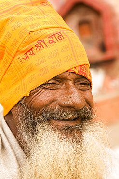 A smiling bearded Indian sadhu wears an orange bandana in Varanasi, Uttar Pradesh, India, Asia