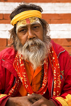 A bearded sadhu wears a bandana and sits by red and white ghats in Varanasi, Uttar Pradesh, India, Asia