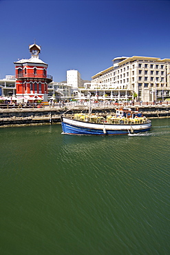 A fishing boat passes the colourful old clock tower in the waterfront in Cape Town South Africa.