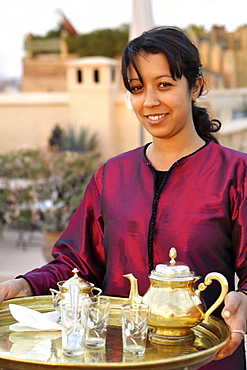 Moroccan girl serving tea on the rooftop of a riad in Marrakech, Morocco