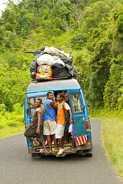 Passengers hanging out the open rear door of a taxi brousse (bush taxi) on the road from Sambava to Andapa in the Antsiranana province of northeast Madagascar, Madagascar, Africa