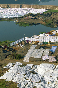 Laundry drying by the Mula River, with foam from detergent pollution beyond, Pune, Maharashtra state, India, Asia