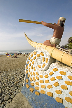 Statue of fisherman with 'caballito (little horse) de totora' reed boat on the beach at the popular far north coast fishing & surfing village of Huanchaco, near Trujillo, Peru, South America