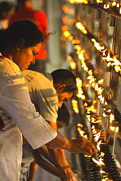 Devotee lighting candles at sunset in the Temple of the Sacred Tooth Relic (Temple of the Tooth), site of Buddhist pilgrimage, Kandy, Sri Lanka, Asia