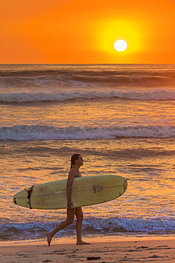 Girl with surfboard at sunset on Playa Guiones surf beach, Nosara, Nicoya Peninsula, Guanacaste Province, Costa Rica, Central America