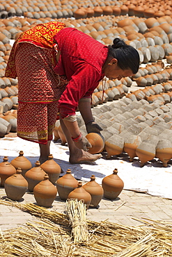 Woman turning pots to dry in sunshine, Potter's Square, Bhaktapur, Nepal, Asia