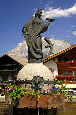 Village fountain with a statue of St. Catherine in front of the Zugspitze massif, Lermoos, Tyrol, Austria, Europe