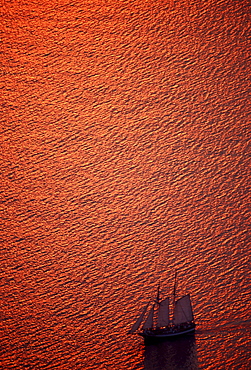 Sailing ship in the gleaming red Mediterranean Sea off the island of Santorini, Cyclades, Greece, Europe