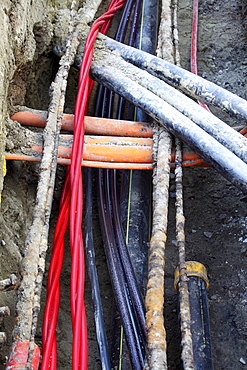 Installation of various cables in a building site, power lines and telecommunication cables, some in protective tubes, placed in the ground