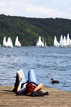 Woman reading a book on the lake shore, 51st Essen Sailing Week on Lake Baldeney, Essen, North Rhine-Westphalia, Germany, Europe