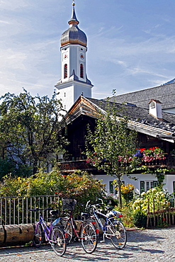 Traditional Bavarian buildings with balconies and flowers, a church behind, Garmisch-Partenkirchen, Bavaria, Germany, Europe