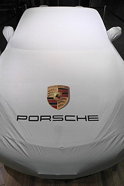 Porsche sports car covered with a white tarp, Porsche's logo and coat of arms