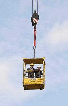 Workers standing inside the raised safety cage of a building crane, industrial safety, construction industry