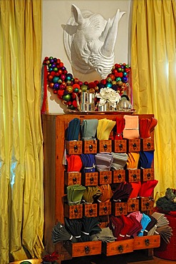 Colourful Christmas baubles and a large, plastic rhino head on a wall above a decorated chest of drawers with colourful napkins for sale, Villa & Ambiente store, Im Weller, Nuremberg, Middle Franconia, Bavaria, Germany, Europe