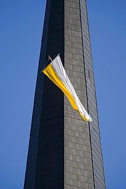 White and yellow flag fluttering from a church tower window against a steel blue sky