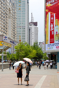 Two women with an umbrella, busy pedestrian zone in the modern city center, Kunming, Yunnan Province, People's Republic of China, Asia