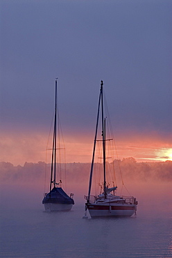 Sun rising behind sailing boats and fog over Ammersee lake, Bavaria, Germany, Europe