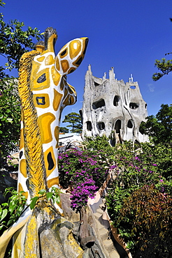 Giraffe statue looking on the bizarre main building of the Crazy House Hotel, Hang Nga Guesthouse, Dalat, Central Highlands, Vietnam, Asia