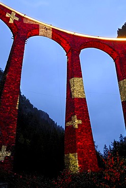 Irrigation water viaduct lit up with the national flag motif to celebrate the acceptance of the "Rhaetische Bahn Railway in Albula/Bernina" as a UNESCO World Heritage Site, Filisur, Graubuenden, Switzerland, Europe