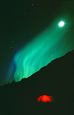 Aurora Borealis over illuminated tent, camping, Chugach Mountains, Alaska, USA