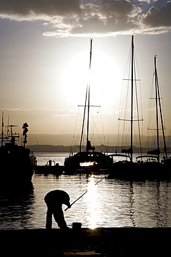 Fisherman silhouetted at the harbour of Syracuse, Sicily, Italy