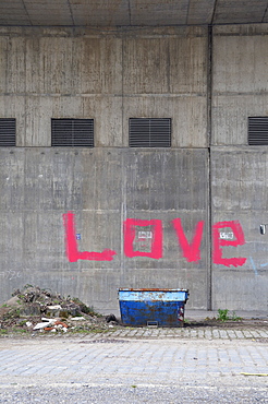 Container in front of a wall with the word love spray-painted in pink