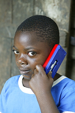 Boy holding a toy mobile phone to his ear, Cameroon, Africa