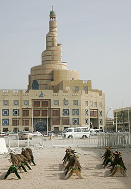 Qatar, Doha, the big tower of the FANAR (Qatar Islamic Cultural Center) building, Arabian architecture, in the foreground falcons are sitting in front of a falconer's shop