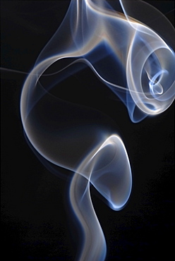 Smoke rising from an incense stick in backlight